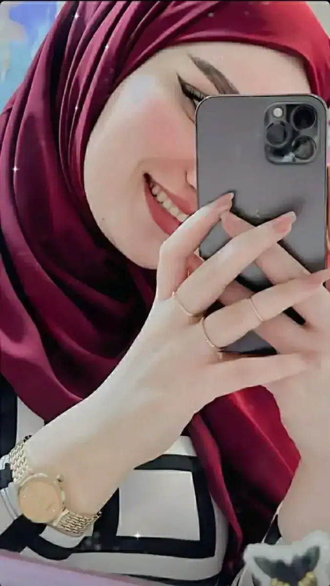 Smiling woman in hijab taking a selfie with a smartphone, showcasing modest fashion and confidence.