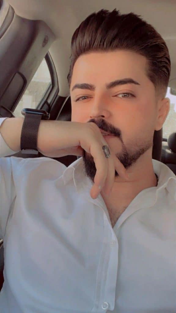 Confident young man with styled hair and beard sitting in car, looking thoughtful.